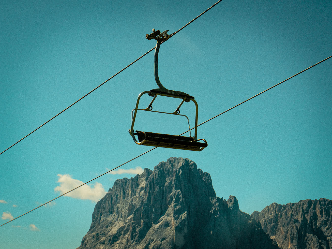 An empty chairlift chair against a bare mountain face