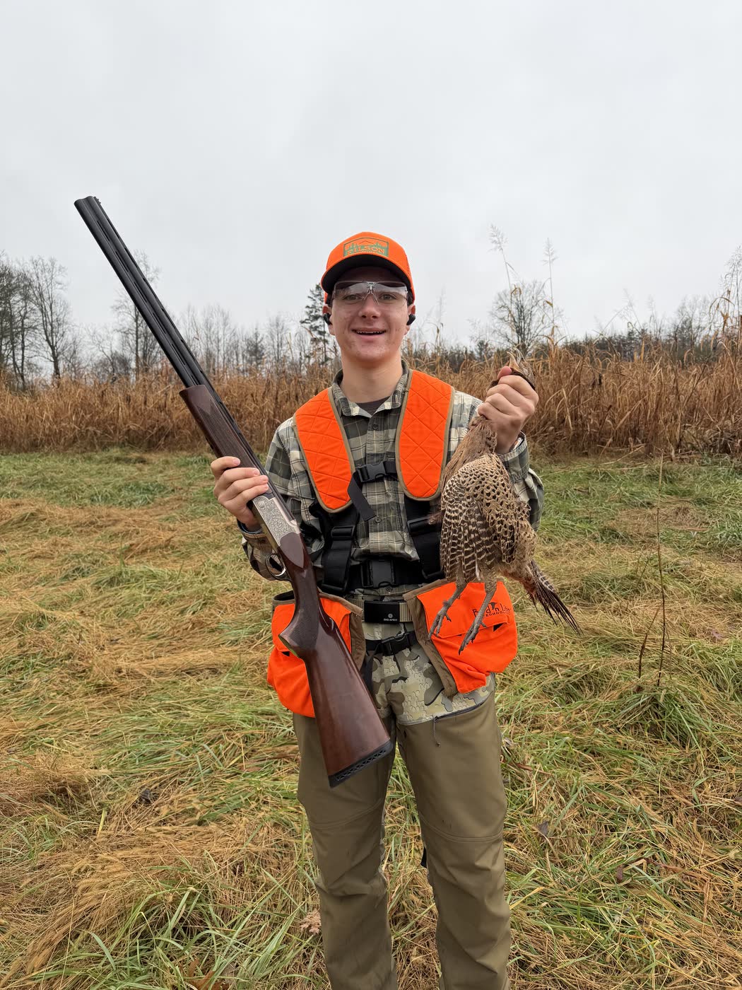 Jack Crombie in blaze orange holding a pheasant after a hunt