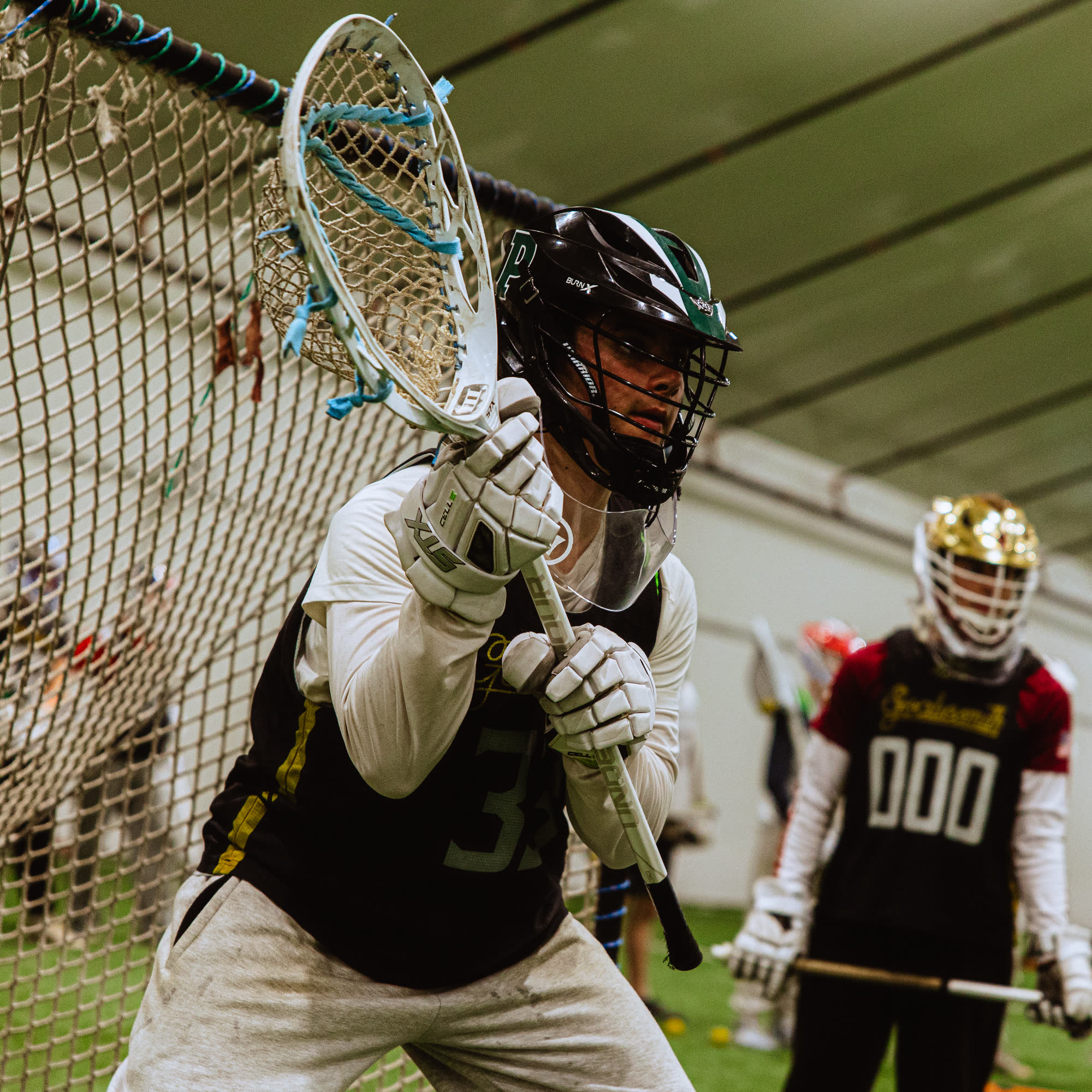 Jack Crombie in goal in a Proctor helmet, stick raised against the net