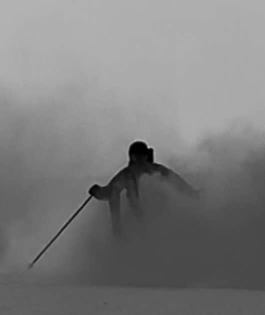 Silhouette skiing into fog and powder spray